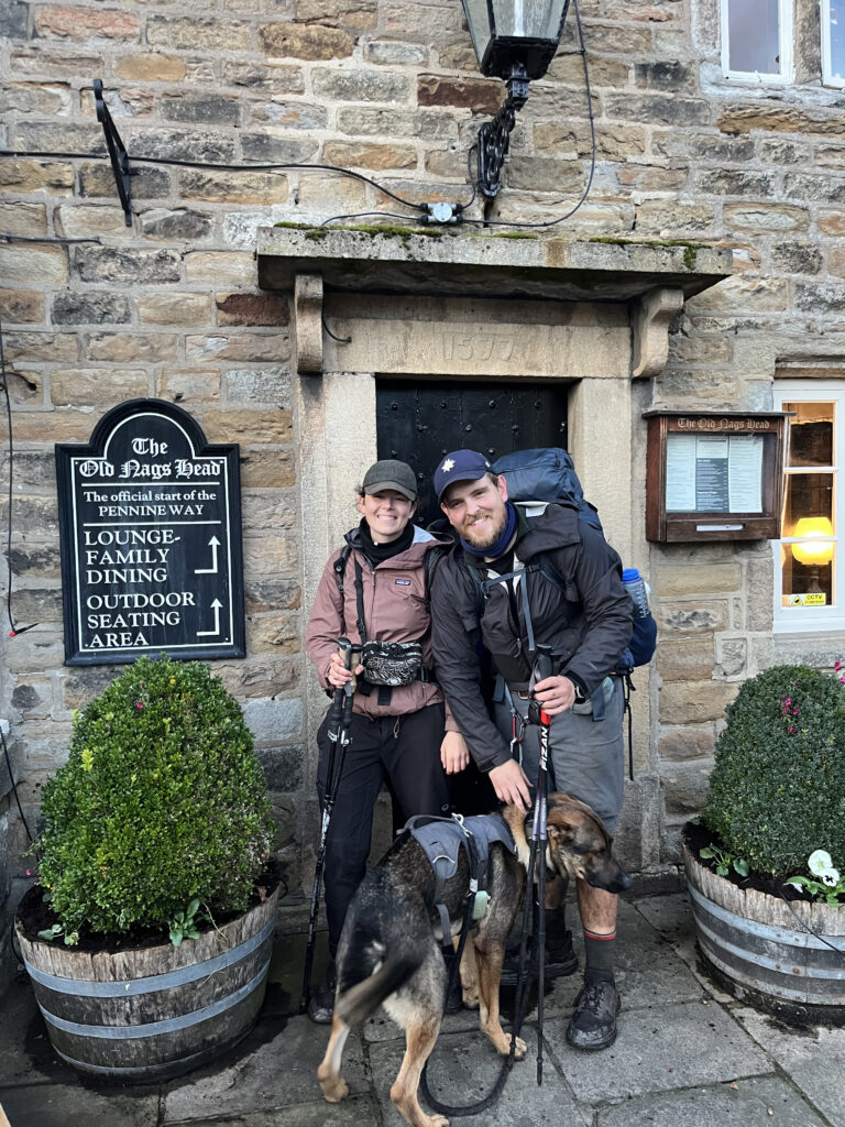 Maresa, Nick & Nero lachend vor dem Pub, dass das Ende auf dem Fernwanderweg Pennine Way ist während der JOGLE Wanderung