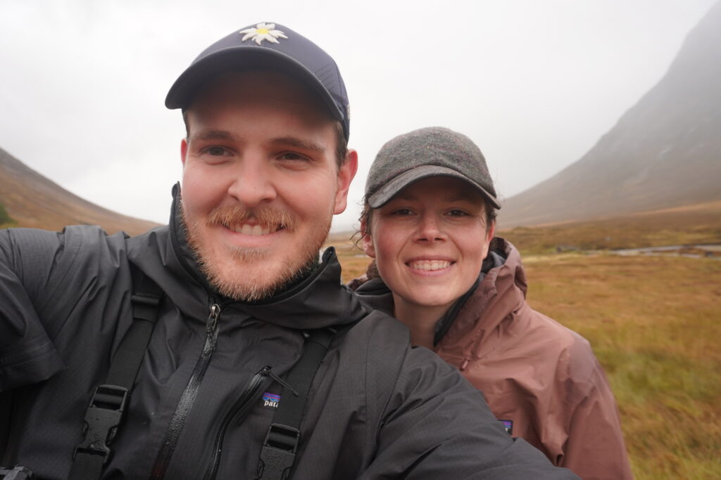 Nick & Maresa lachen frontal in die Kamera während sie auf dem West Highland Way unterwegs sind.