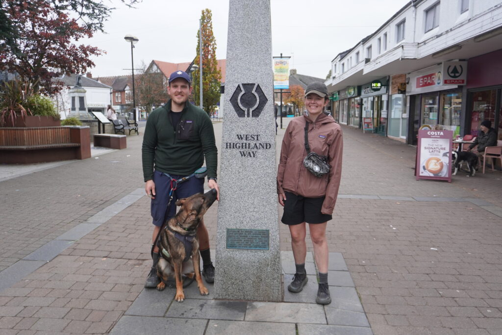 Maresa und Nick mit Hund vor dem Obelisk am Ende des West Highland Way in Milngavie bei Glasgow