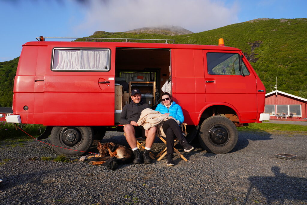 Nick, Maresa und Hund Nero sitzend vor einem alten Feuerwehrauto.