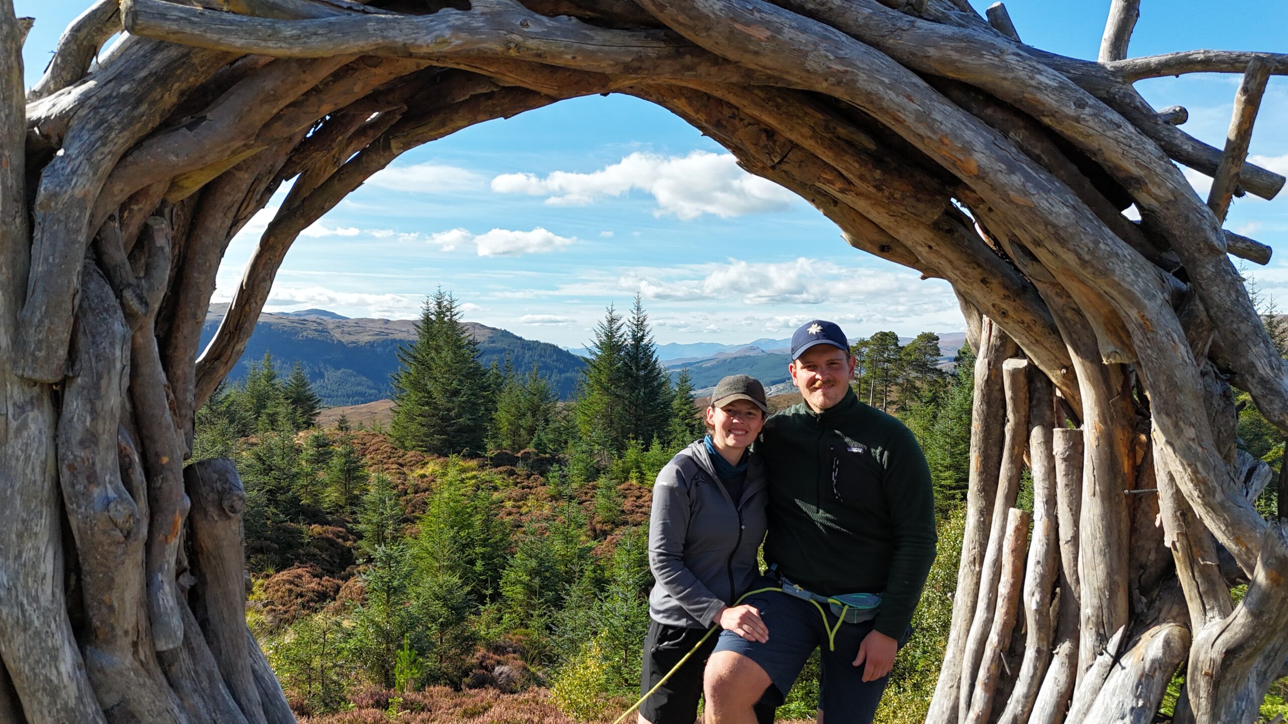 Nick und Maresa posierend vor einer sonnigen Landschaft mit Bergen während ihrer JOGLE Fernwanderung durch Großbritannien