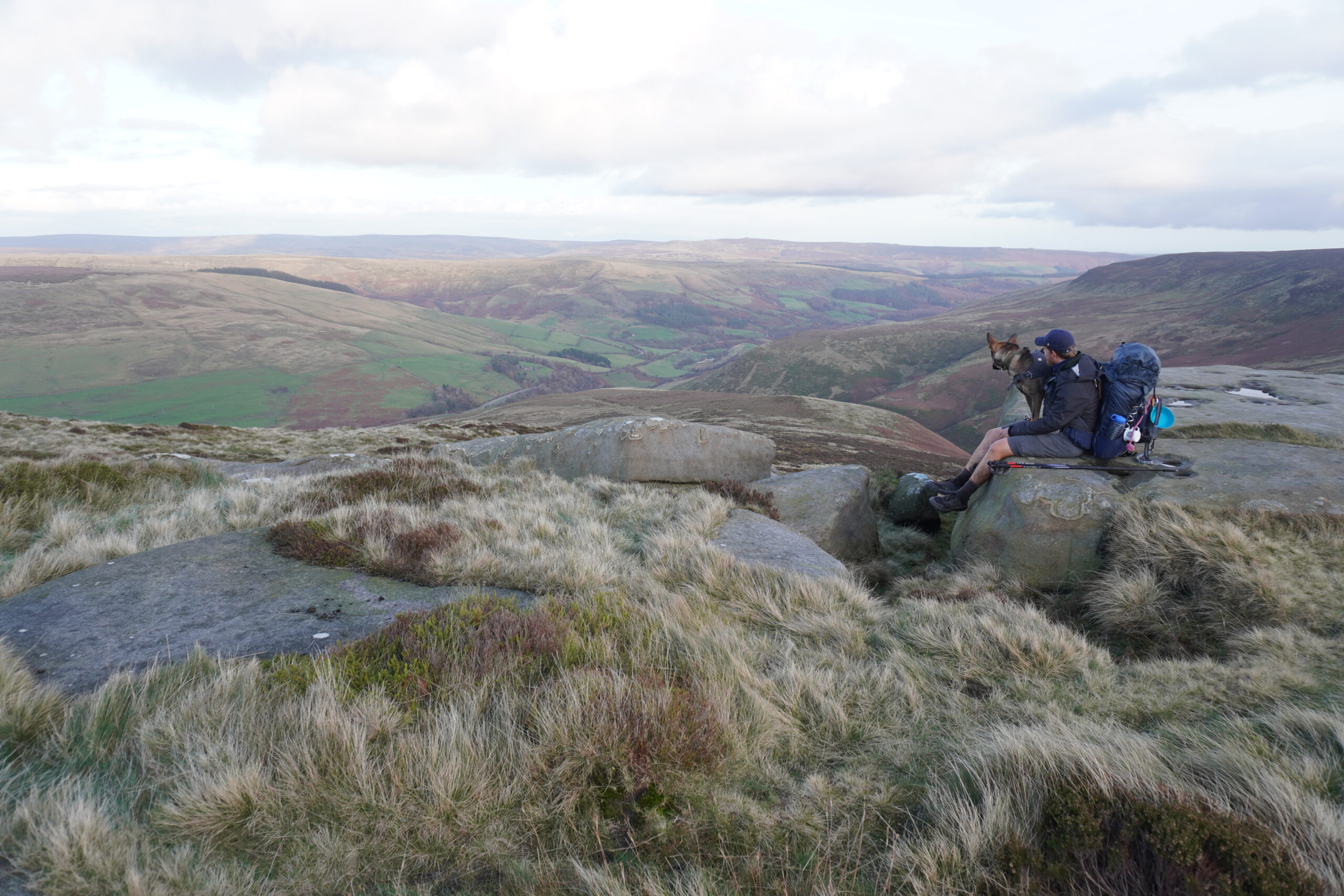 Nick und Nero sitzend auf einem Steinvorsprung mit einer Aussicht auf die hügelige Landschaft des Pennine Way während der JOGLE Wanderung